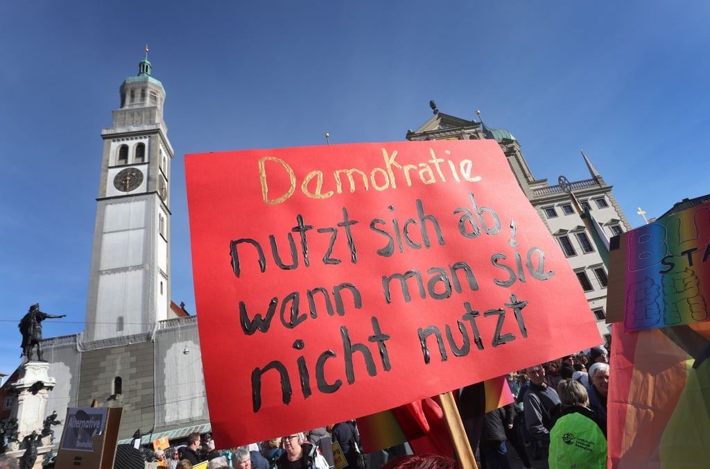 Demonstranten halten auf dem Rathausplatz ein Schild mit der Aufschrift "Demokratie nutzt sich ab, wenn man sie nicht nutzt".
