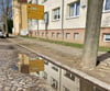 Ein Wohnblock an der „Froschvilla“ spiegelt sich in einer Pfütze der maroden Bahnhofstraße. Die Straße und der Gehweg sollen in mehreren Bauabschnitten saniert werden.