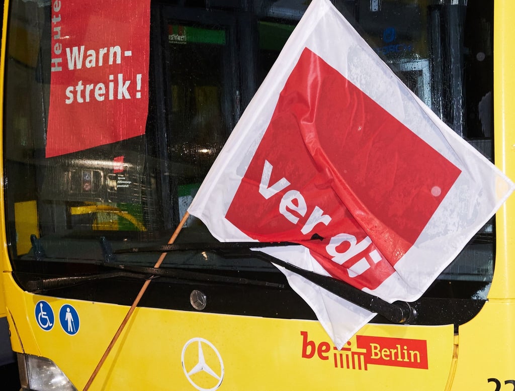 Ein Bus mit einer Verdi-Fahne steht hinter einer Schranke.