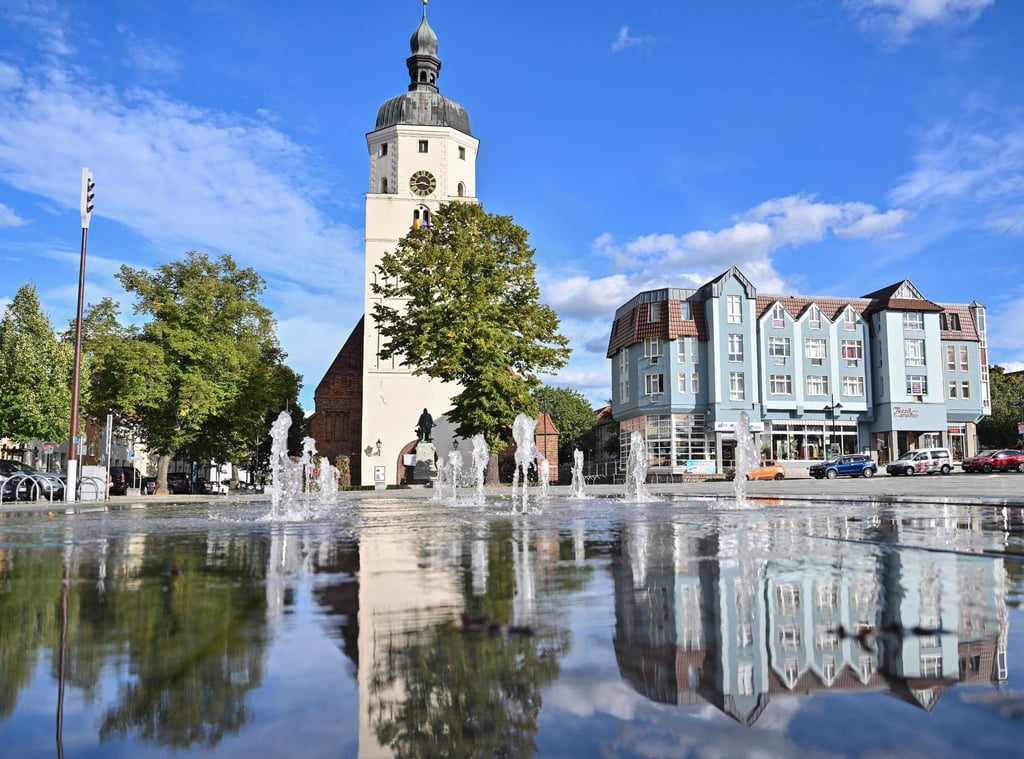 Die Paul-Gerhardt-Kirche und Wohnhäuser am Markt der brandenburgischen Kreisstadt Lübben spiegeln sich in einem Brunnen.