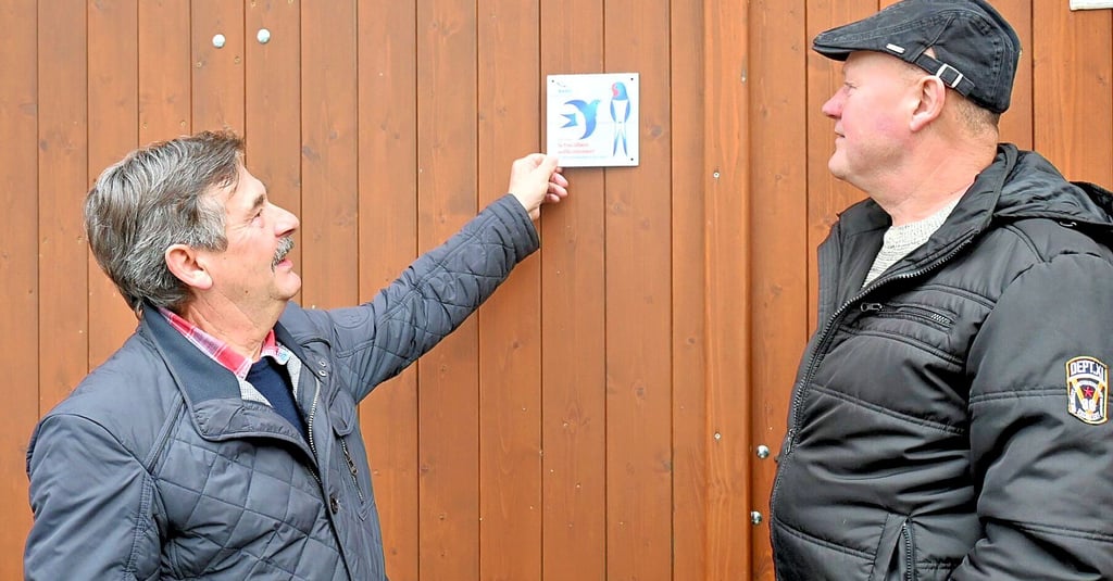 Werner Ackermann (links) bringt stolz die Plakette am Hoftor an, die das Grundstück als schwalbenfreundlich ausweist. Hobby-Ornithologe Holm Ramisch aus Klein Oschersleben hat ihn bei der Beantragung der Auszeichnung unterstützt.