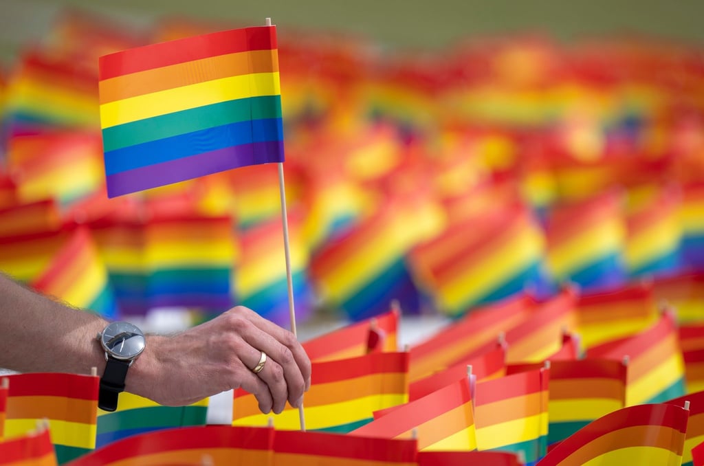 Ein Mann hält ein Regenbogenfähnchen in der Hand.