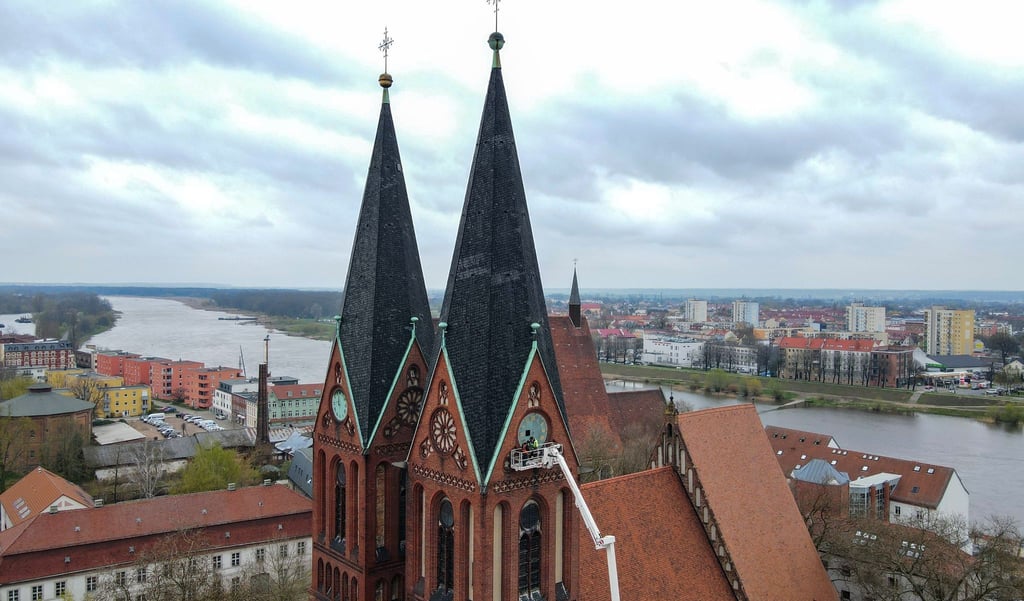 Zwei Mitarbeiter von der Firma Bittner Glocken- und Turmuhren sowie ein Techniker der Hebebühne montieren in 38 Metern Höhe die vergoldeten Zeiger und Ziffern an der südlichen Turmuhr der Friedenskirche.