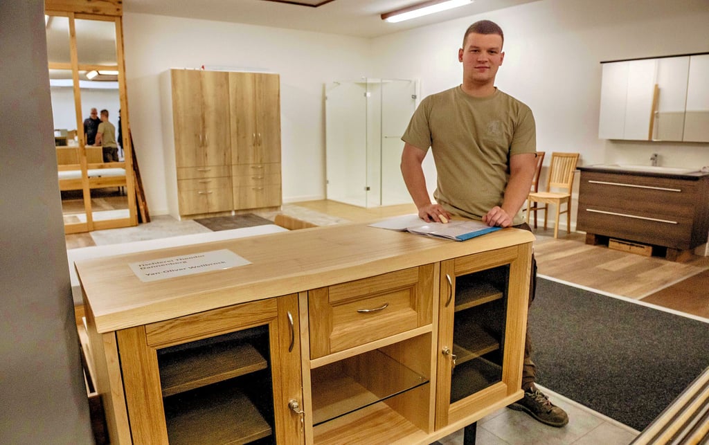 Yan-Oliver Wellbrock steht neben seinem Gesellenstück, einem Sideboard auf Stahlfüßen.