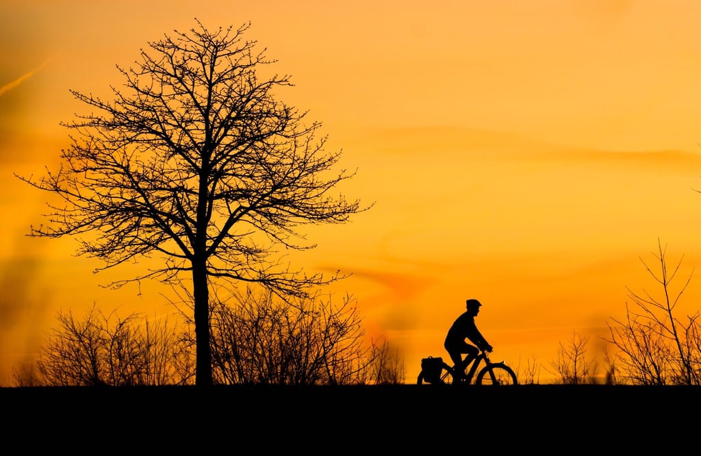 Ein Mann fährt bei Sonnenaufgang mit einem Fahrrad über einen Feldweg in der Region Hannover.