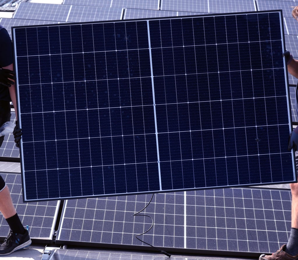 Monteure tragen ein Solarmodul auf einem Dach.