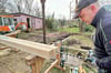 Vorarbeiter Dirk Baumann von der Zimmerei Meißner bohrt Löcher in die Stützbalken, aus denen neben dem Flamingohaus (hinten in Pink) die Einhausung für einen Brunnen  gebaut wird.