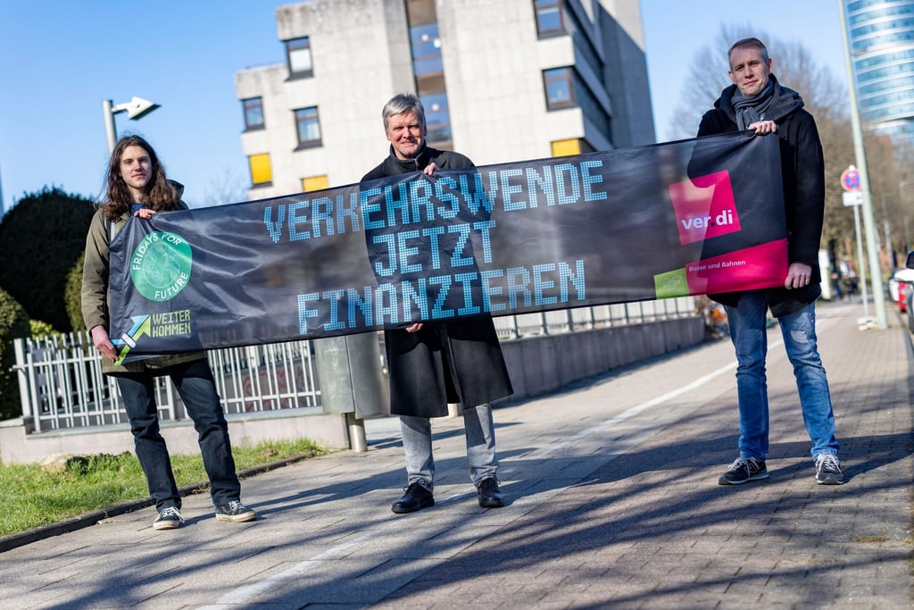 Emil Görtzen (l-r) von Fridays for Future, Jürgen Schirmer von Verdi und Patrick Steinbach vom Verkehrsbetrieb BoGeStra stehen mit einem Banner zum gemeinsamen Aktionstag vor der Verdi-Zentrale in Bochum.