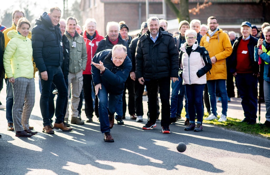 Stephan Weil (SPD), Ministerpräsident von Niedersachsen, wirft eine Boßelkugel über die Straße.