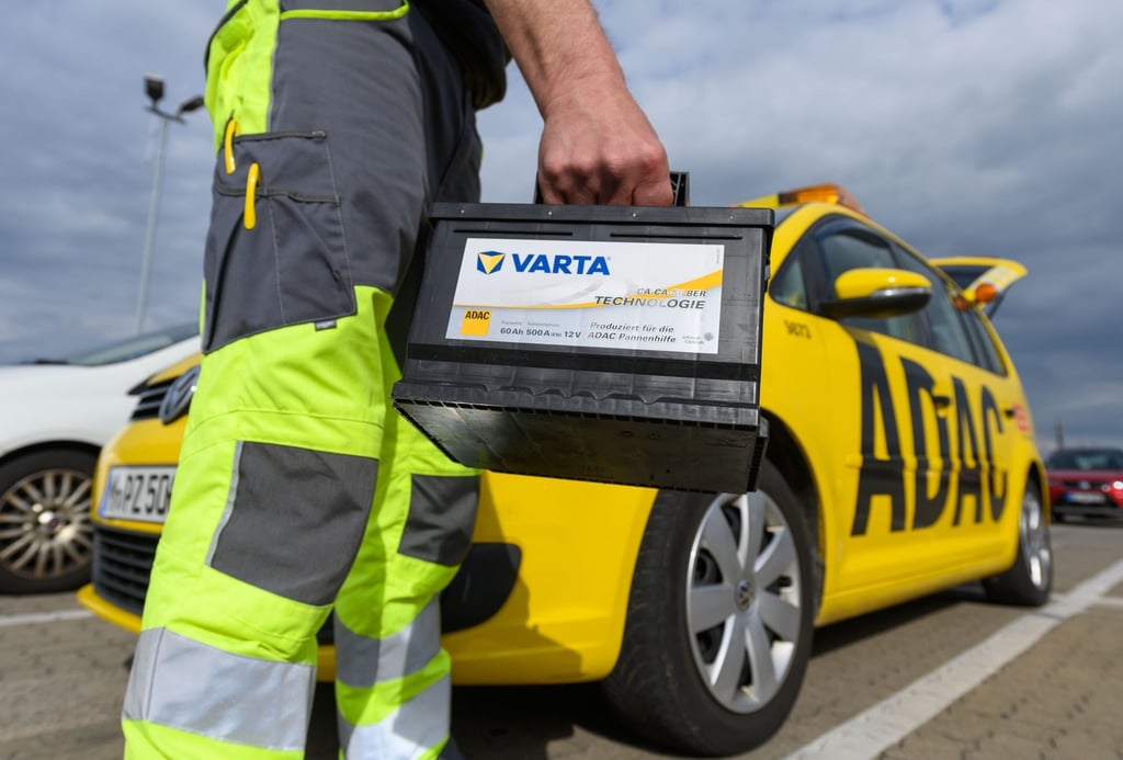 Ein Pannenhelfer der ADAC-Straßenwacht hält vor seinem ADAC Auto eine Autobatterie.