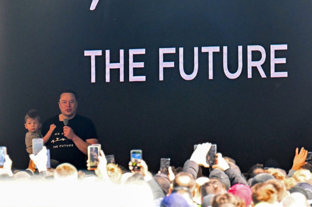 Tesla-Chef Elon Musk spricht in der Tesla Gigafactory Berlin-Brandenburg zu den Mitarbeitern und hält dabei ein Kind auf dem Arm.