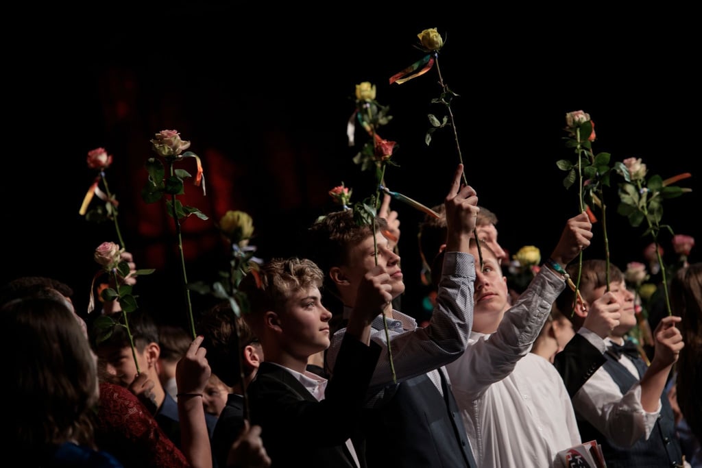 Teilnehmer der Jugendfeier des Humanistischen Verbands Berlin-Brandenburg schwenken Rosen auf der Bühne bei der Festveranstaltung.
