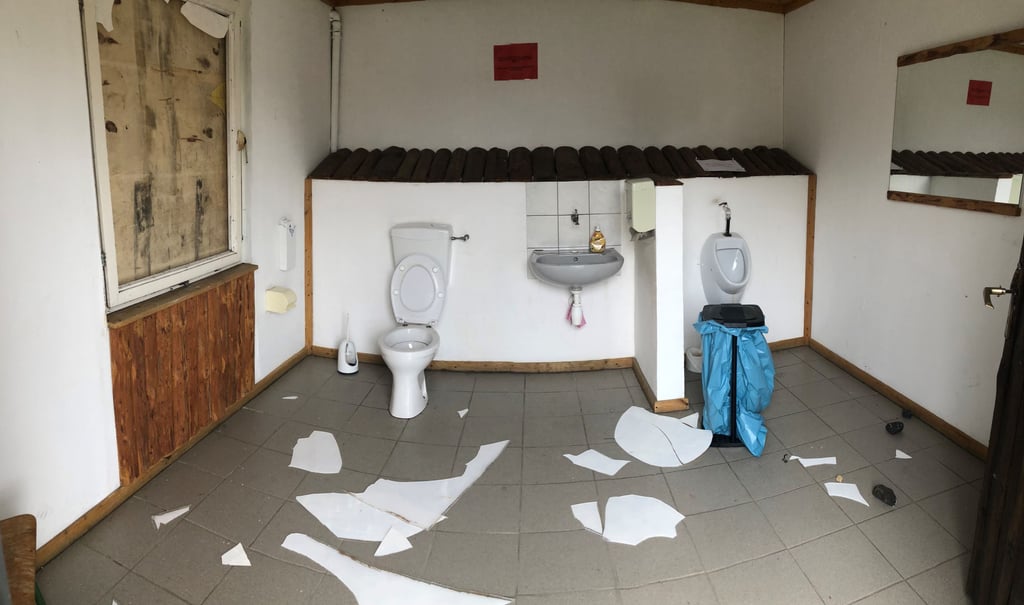 Blick in den Toilettenraum der Wetterschutzhütte, wo Scherben und Steine nach der mutwilligen Zerstörung des Fensters noch auf dem Boden liegen.