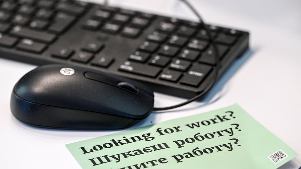Auf einer Jobmesse liegt ein Werbezettel, auf dem in drei Sprachen „Suchen sie Arbeit?“ gedruckt ist.