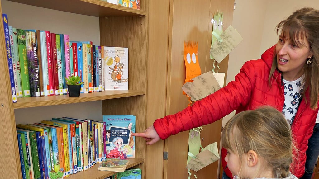 Katharina Grünig zeigt der Zweitklässlerin Leni die Bücher, die sich die Schülerin ausleihen kann.