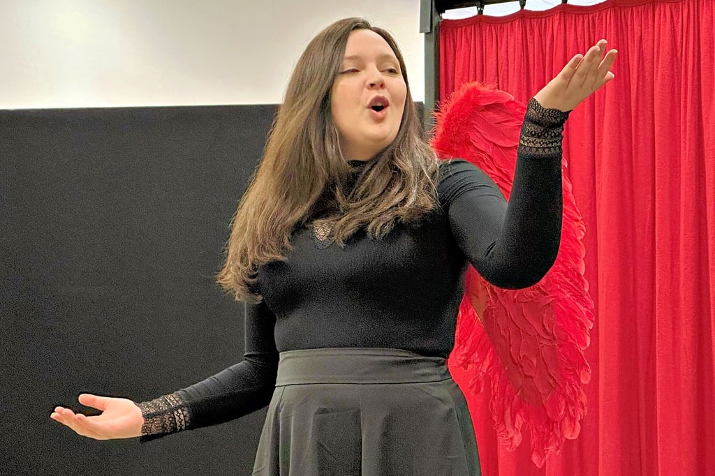 Im schwarzen Gewand und mit roten Engelsflügeln tritt Amora, gespielt von Sarah Kowallik, auf die Bühne. Sie führt als mythische Figur durch die Geschichten der Magdeburg-Soap „Liebestoll“.
