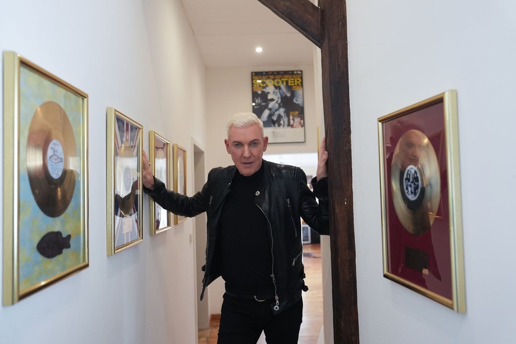 Der Musiker H.P. Baxxter steht in einem Flur in seinem Musikstudio neben zahlreichen goldenen Schallplatten.