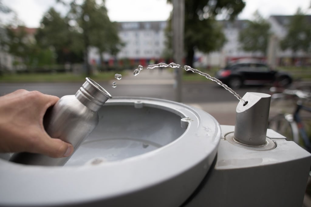 An einem Wasserspender füllt sich ein Passant seine Trinkflasche mit Wasser auf.