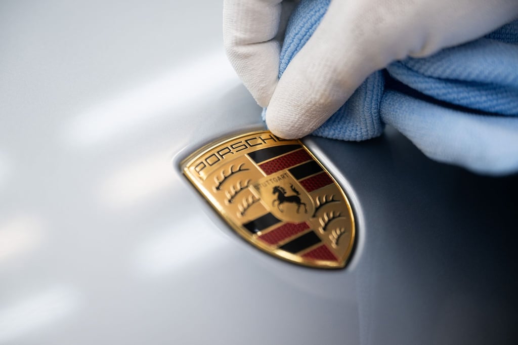 Ein Mitarbeiter der Porsche AG reinigt im Stammwerk in Zuffenhausen das Porsche-Wappen auf einer Motorhaube.