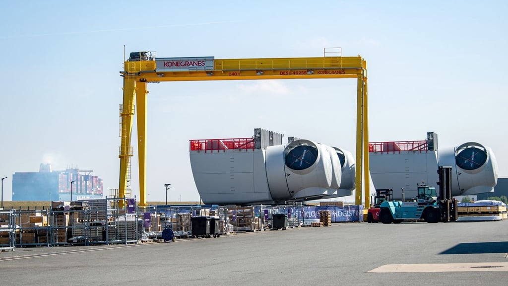 Ein Containerschiff fährt an den Offshore-Maschinenhäusern auf dem Werkgelände von Siemens Gamesa in Cuxhaven vorbei.