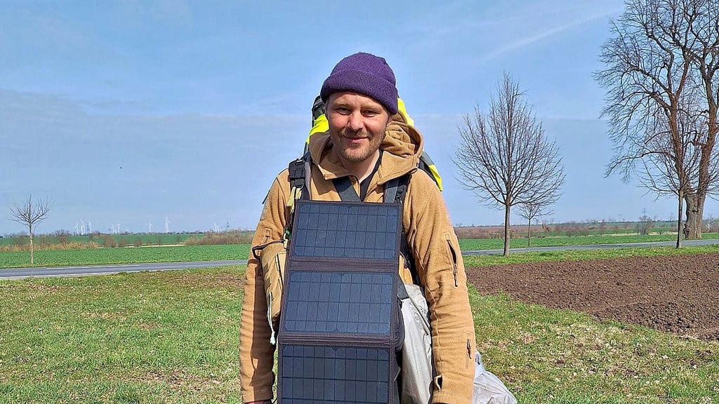 Tobias Nied läuft von Köln nach Leipzig. Dabei hat er auch den Saalekreis passiert und in Schafstädt am Fuße eines Windrades übernachtet. Vor seinem Bauch hat er Solarpanele, mit denen er sein Handy lädt.