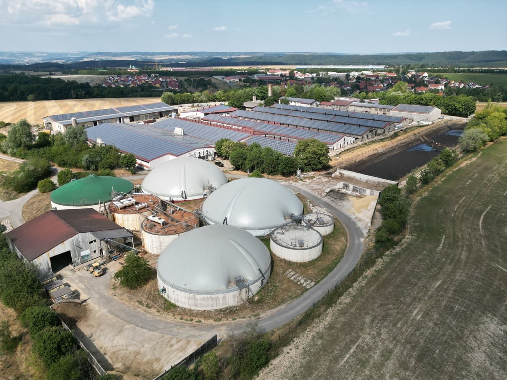 Blick auf eine Biogasanlage einer Agragenossenschaft. Dahinter sind Gebäude mit Solarpanelen zu sehen.