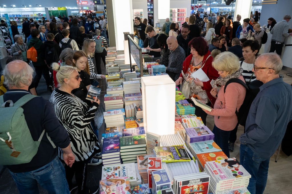 Besucherinnen und Besucher der Leipziger Buchmesse schauen sich einen Bücherstand an.