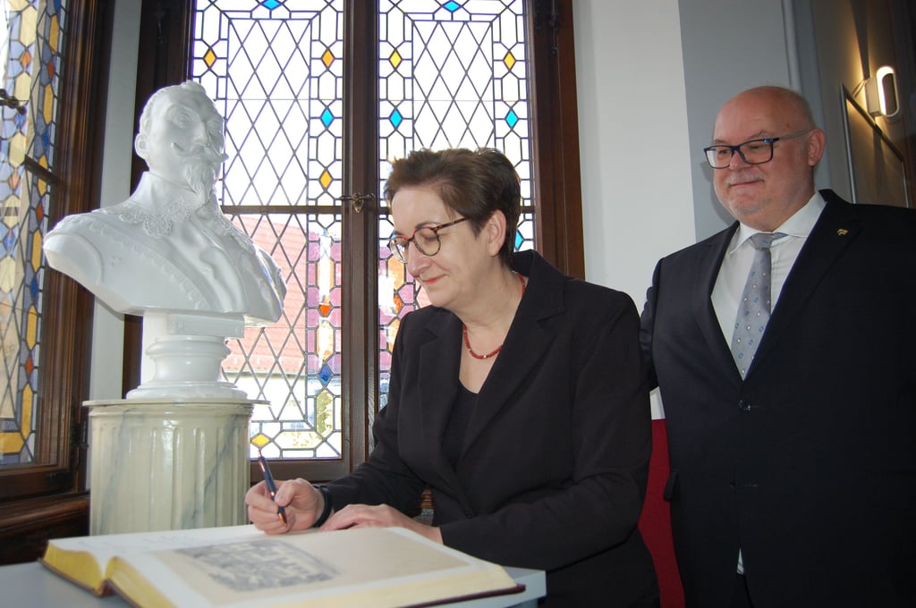 Ministerin Klara Geywitz trägt sich unter den Augen von Bürgermeister Uwe Weiß ins Goldene Buch der Stadt Lützen ein.