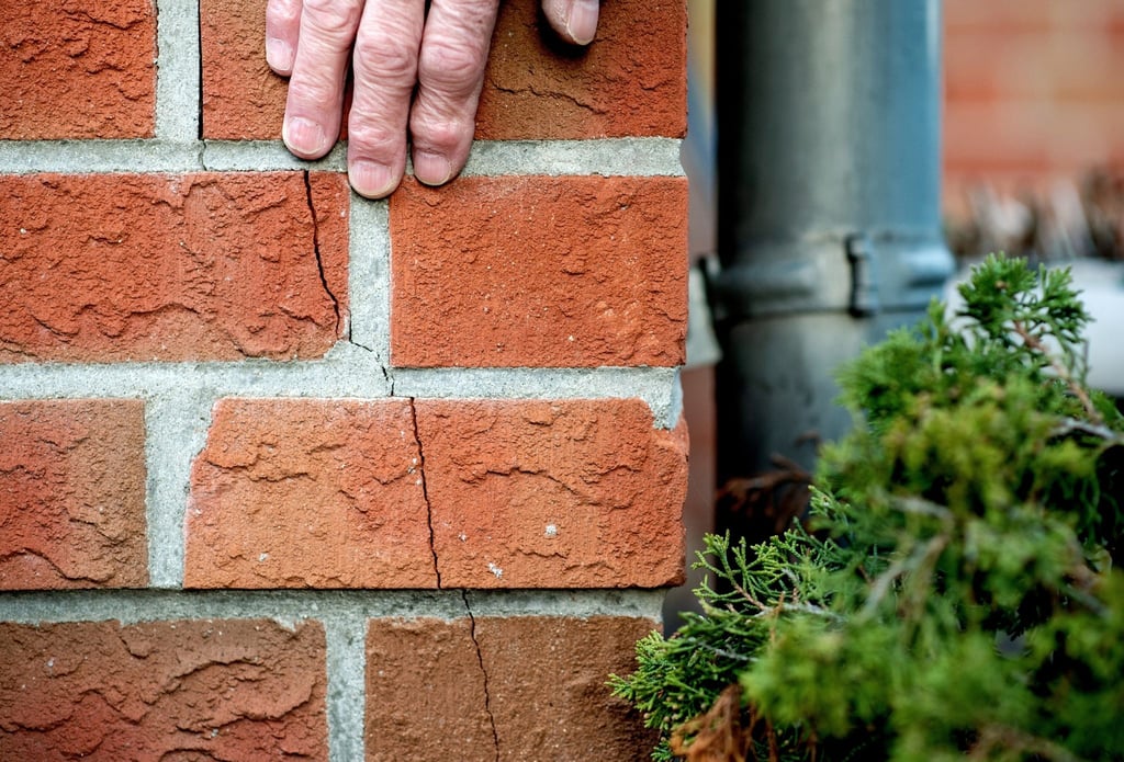Ein Mann streicht mit seiner Hand über den durch ein Erdbeben entstanden Riss am Haus.