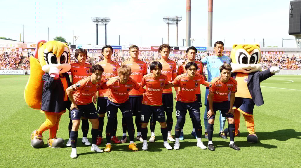Mannschaft von Omiya Ardija mit den Maskottchen Ardy (rechts) und Miya (links).