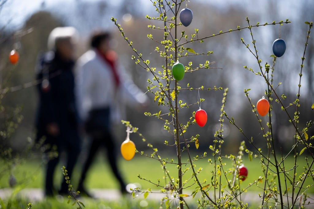 Zwei Menschen laufen an aufgehängten Ostereiern vorbei im Britzer Garten.