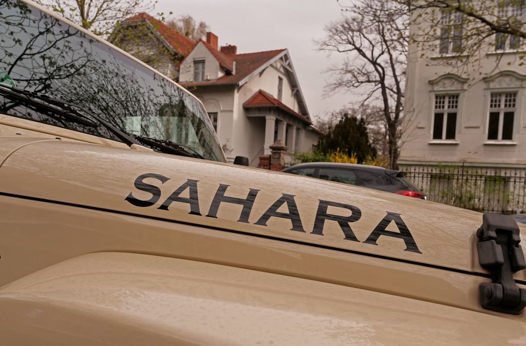 Ein sandfarbener Jeep mit der Aufschrift „Sahara“ steht bei dunstigem Licht in einer Straße der Hauptstadt.