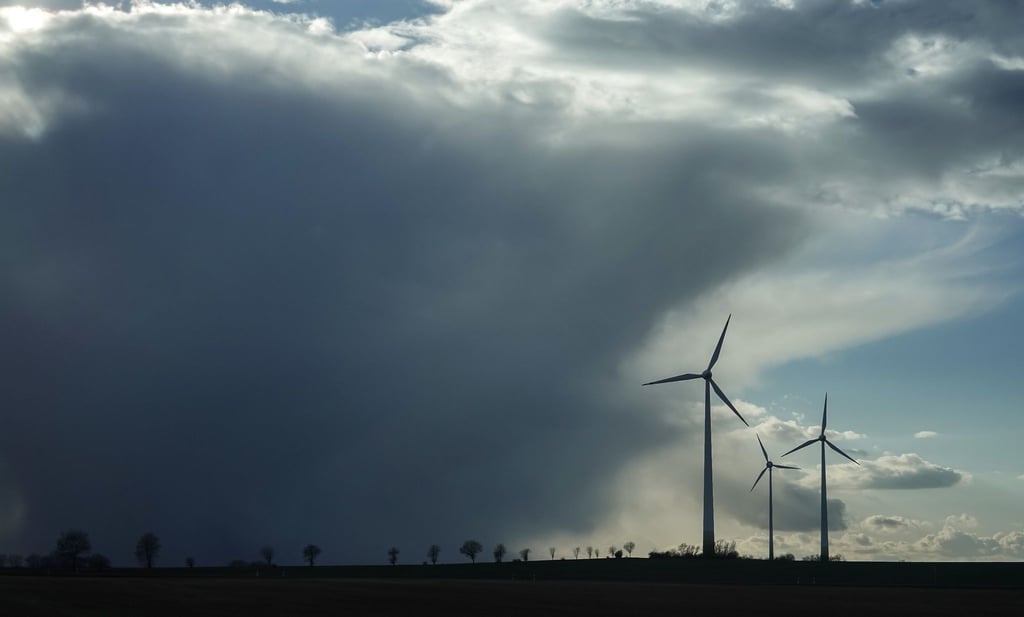 Ein Regenschauer zieht über eine Landschaft mit Windrädern hinweg.