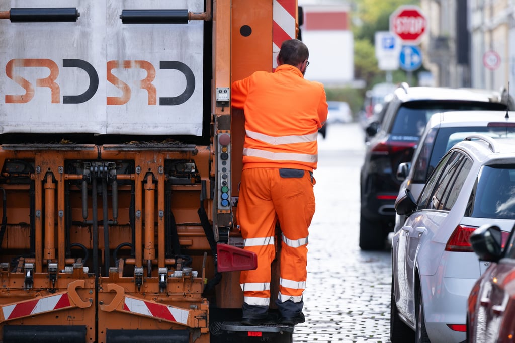 Ein Müllmann stehend an der Rückseite eines Müllfahrzeugs.