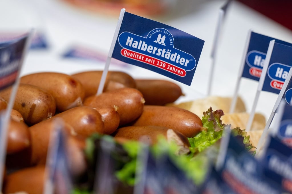 Ein Papierfähnchen mit dem Logo der Marke Halberstädter steckt in einem Würstchen am Stand des Herstellers auf der Grünen Woche.