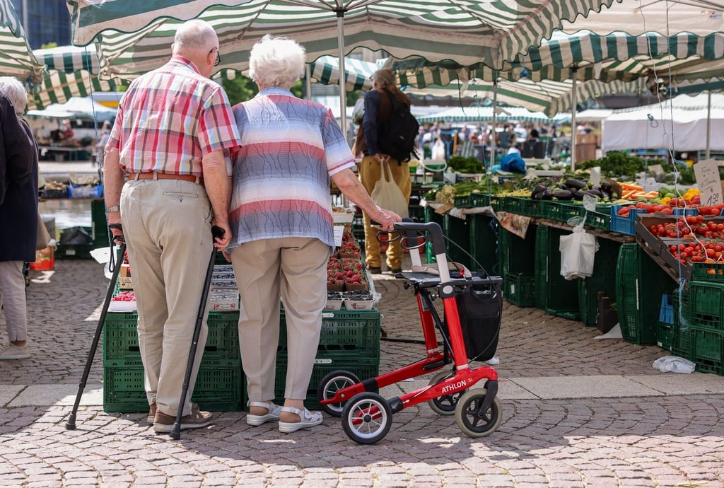 Zwei Senioren stehen mit Gehhilfen und Rollator auf dem Wochenmarkt in der Leipziger Innenstadt.