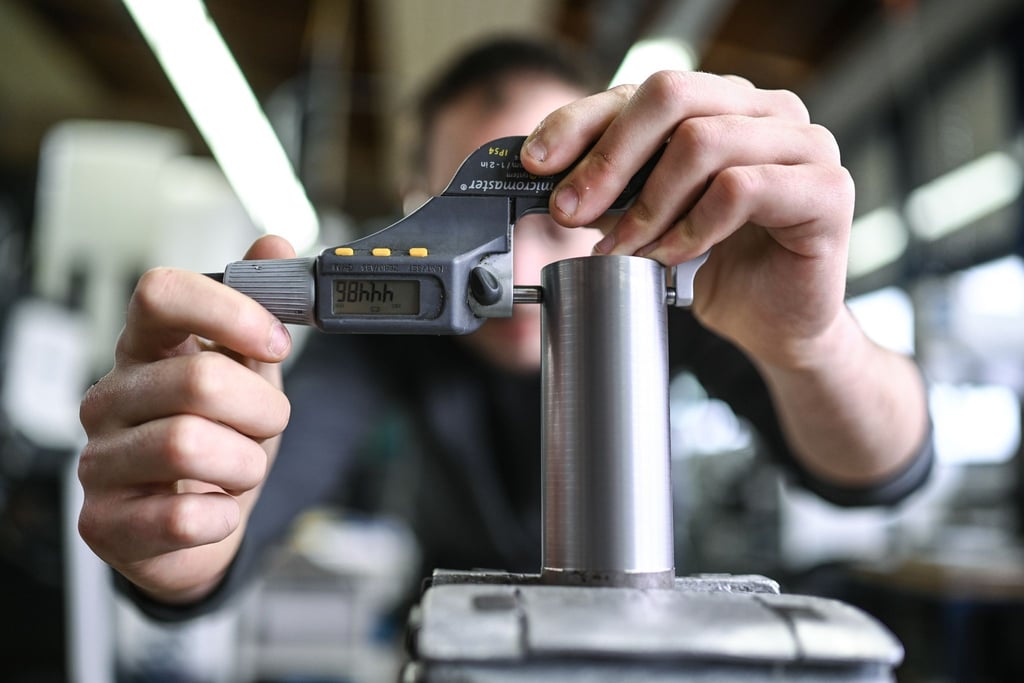 Ein Auszubildender im Metall-Handwerk misst in einem Ausbildungszentrum die Dicke eines Werkstücks.