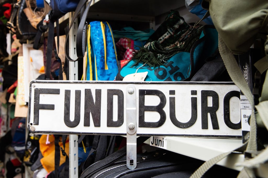 Ein Schild mit der Aufschrift „Fundbüro“ steht zwischen Rucksäcken und Taschen in einem Regal.