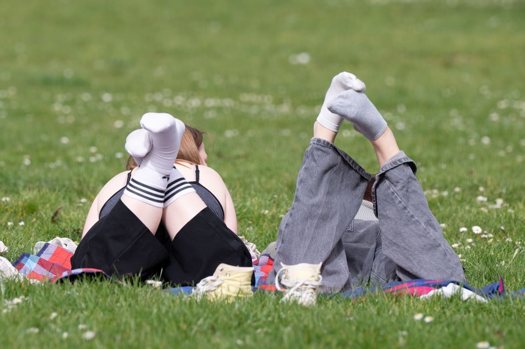 Zwei Personen liegen auf einer Wiese in der Sonne. Zum Wochenende werden Rekordtemperaturen erwartet.