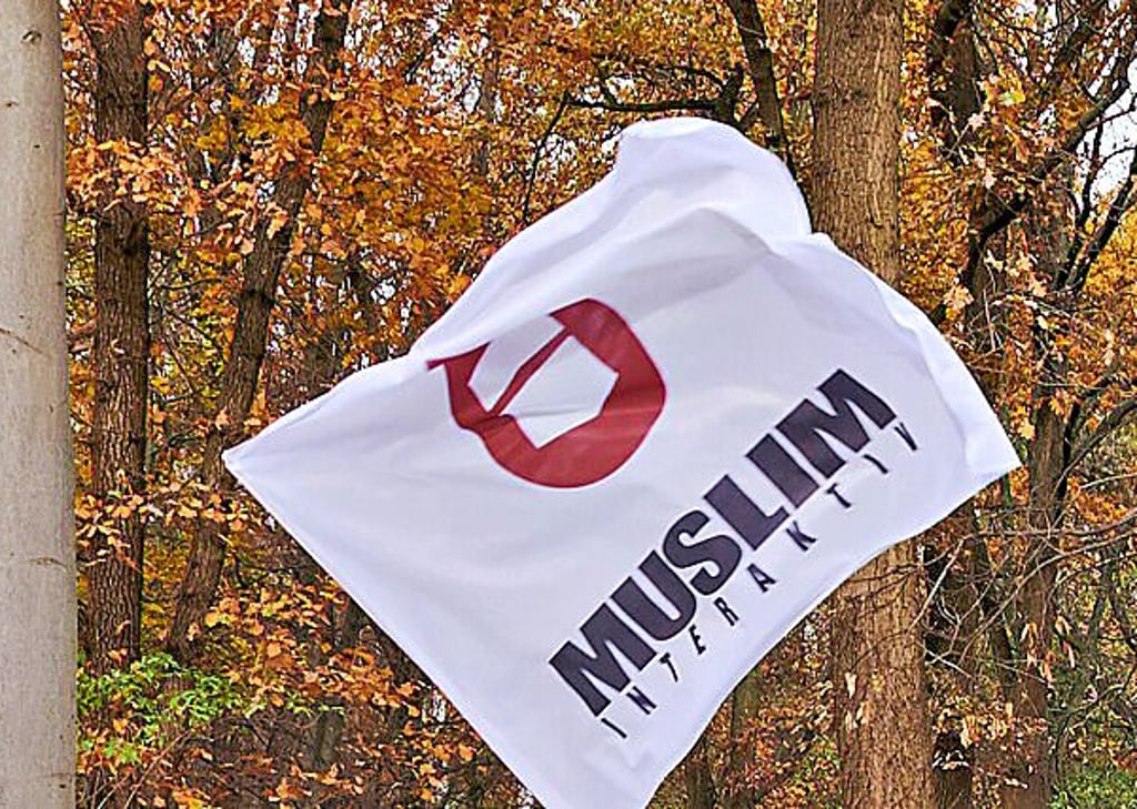 Eine Fahne von „Muslim Interaktiv“ hängt vor einem Baum.