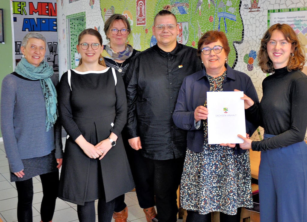 Ministerin Petra Grimm-Benne (2. von rechts) überreicht Mika Taube und Lea Arnold (rechts) vom Jugendnetzwerk Lambda Mitteldeutschland den Zuwendungsbescheid in der Kleinen Markthalle in Stendal.