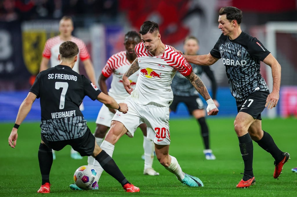 Leipzigs Spieler Benjamin Sesko (M) versucht, sich gegen Freiburgs Noah Weisshaupt (l) und Nicolas Höfler durchzusetzen.