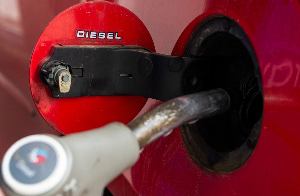 Eine Person hält einen Zapfhahn in die Tanköffnung seines Fahrzeugs um an einer Tankstelle Diesel zu tanken.