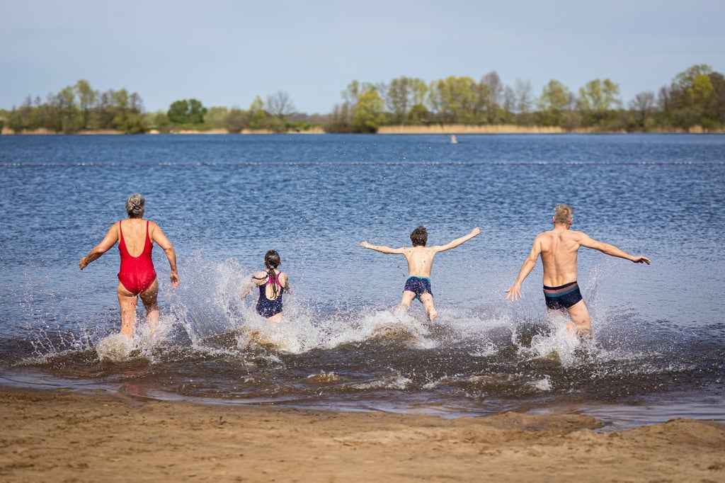 Eine Familie läuft bei sonnigem Wetter in den Hufeisensee in der Region Hannover.