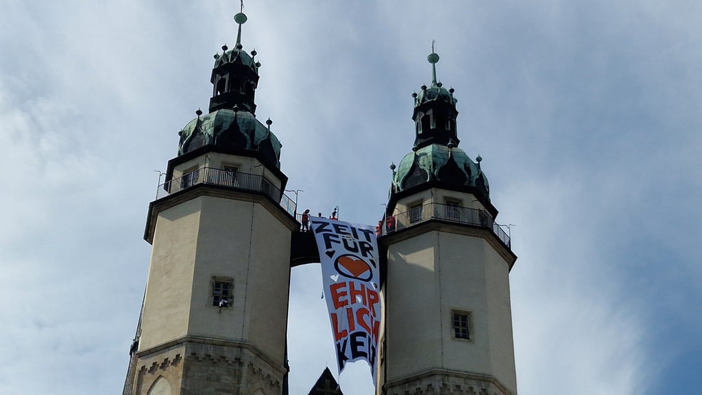 Ein  großes Banner von Umweltaktivisten von "Letzte Generation" hängt von den Hausmannstürmen der Marktkirche in Halle  herab.