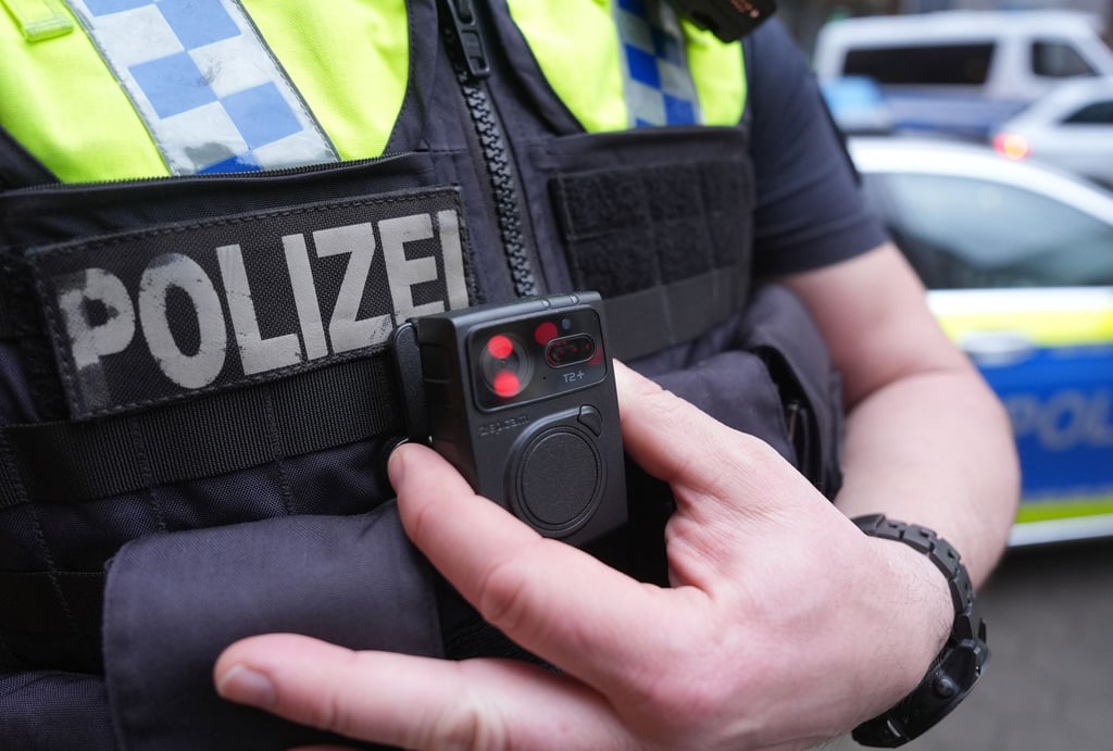 Ein Polizist greift an eine Bodycam an seiner Weste.