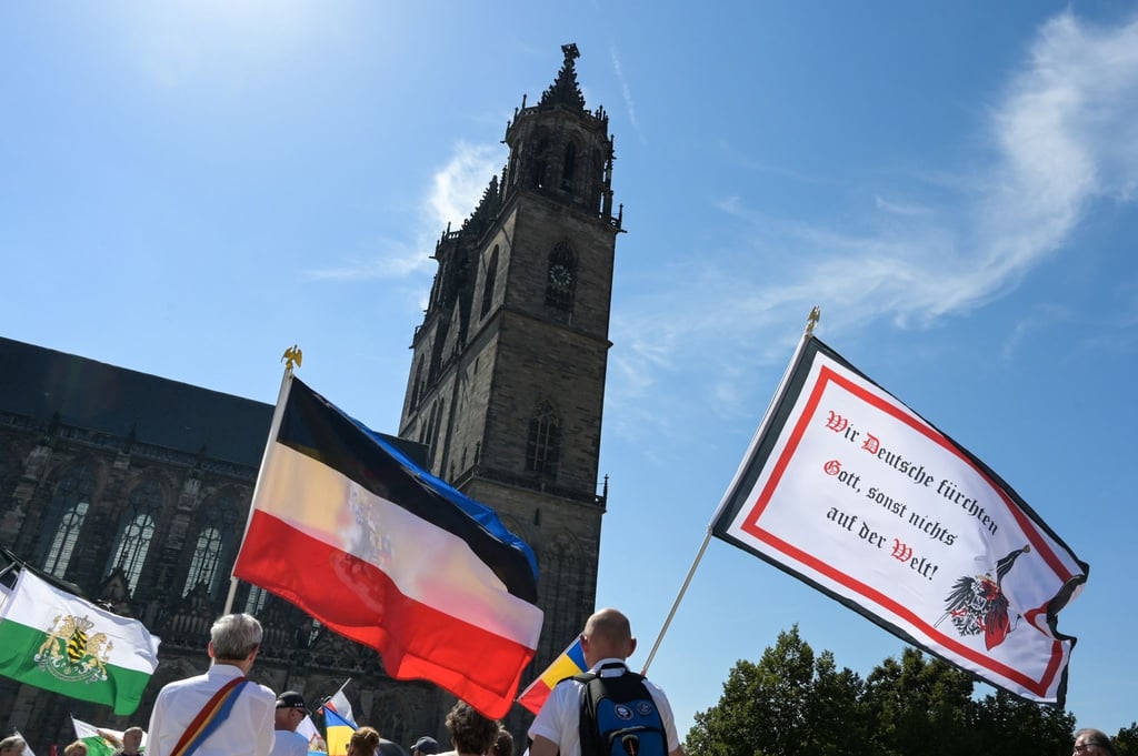 Die Reichsflagge und eine Fahne mit der Aufschrift "Wir Deutschen fürchten Gott, sonst nichts auf der Welt" wird vor dem Magdeburger Dom bei einer Demonstration der „Reichsbürger“-Szene hochgehalten.