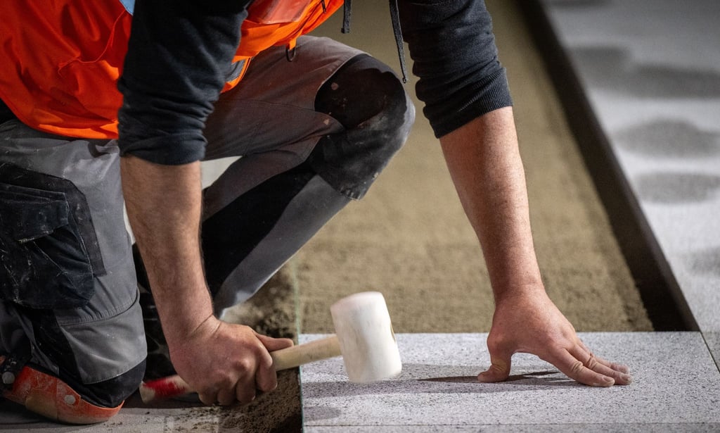 Ein Bauarbeiter verlegt mit einem Gummihammer den Bodenbelag auf einer Baustelle.