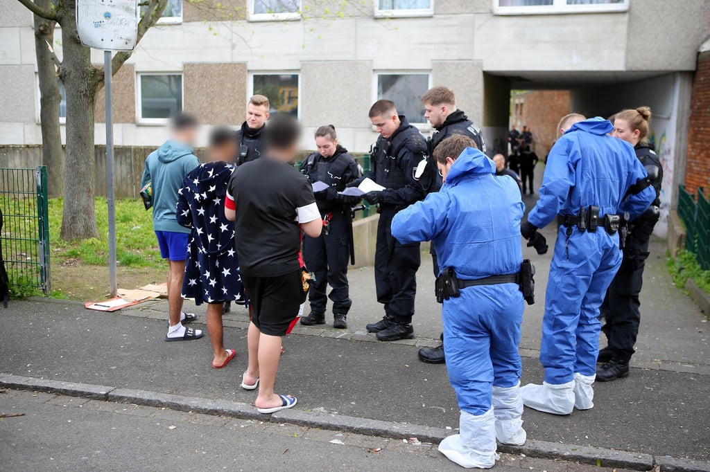Polizisten, zum Teil in Schutzkleidung, kontrollieren Anwohner vor einem Wohnkomplex.