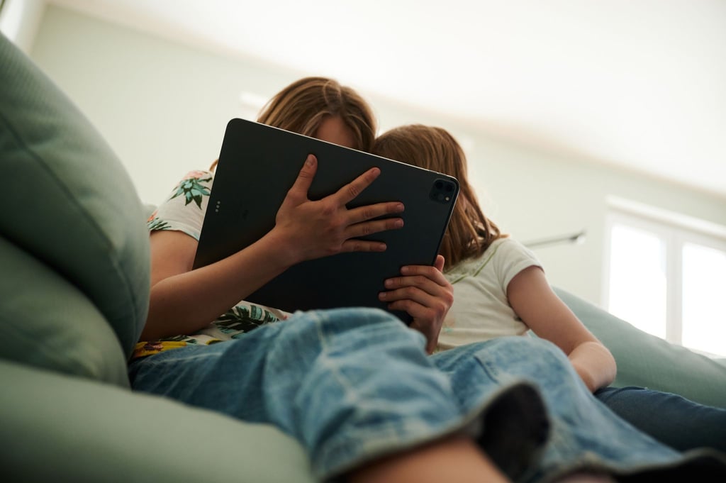 Zwei Schwestern sitzen auf der Couch und gucken in das Tablet ihrer Eltern.